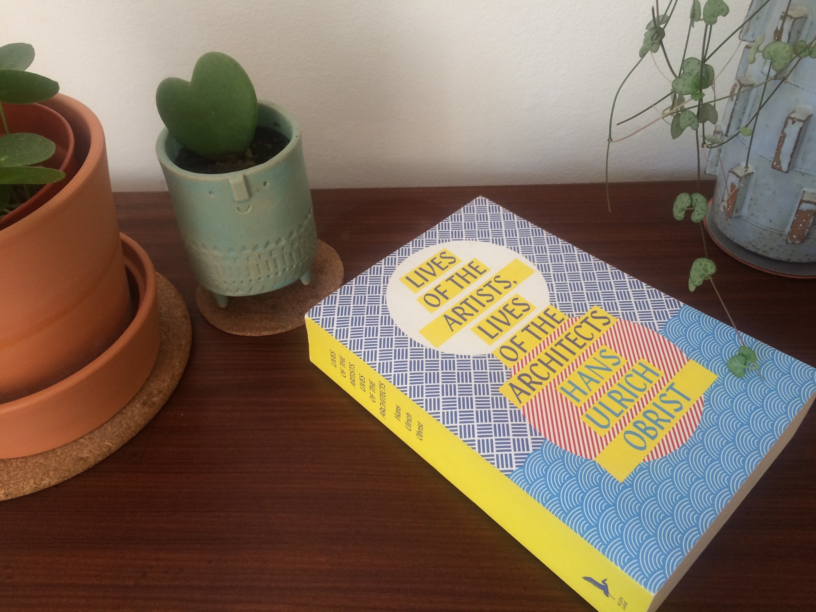 Lives of the Artists, Lives of the Architects by Hans Ulrich Obrist Photograph of the book Lives of the Artists, Lives of the Architects by Hans Ulrich Obrist on a sideboard surrounded by plant pots.
