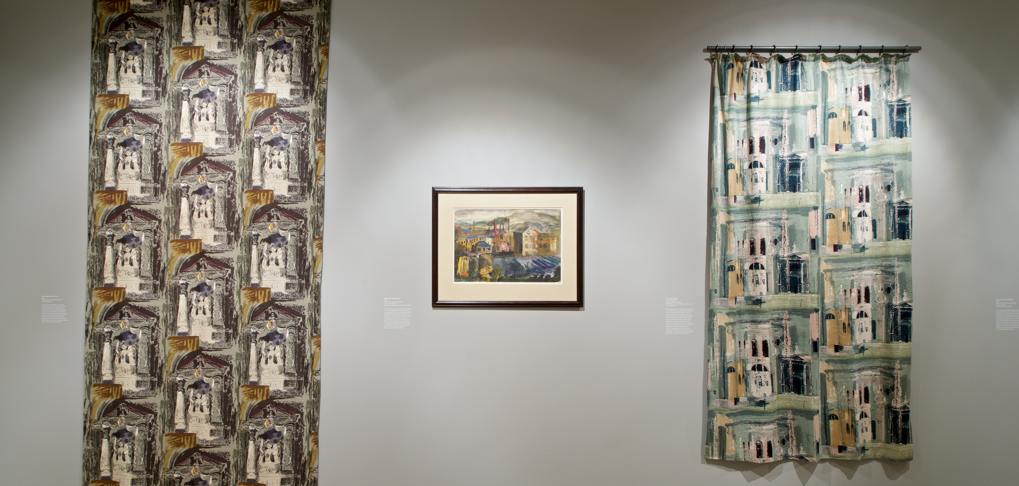 Photograph Mark Heathcote View of interior of gallery showing two lengths of cloth with two different abstract designs. Between them is a painting showing a mid-century urban landscape.