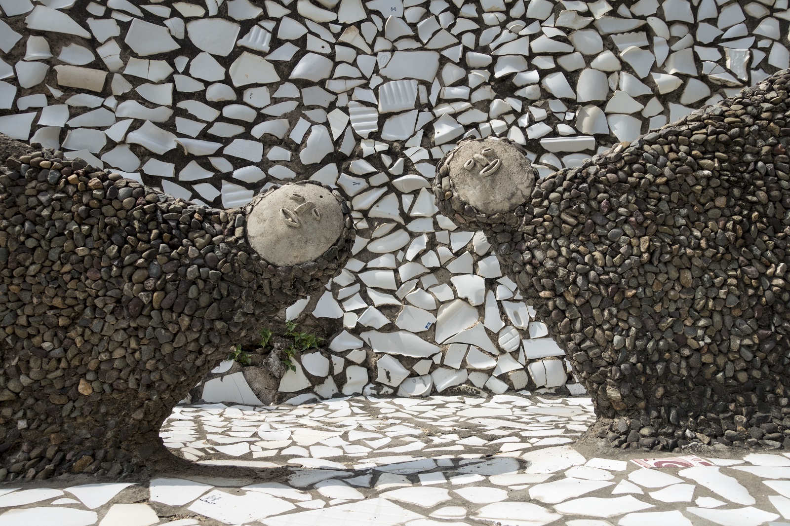 Nek Chand, The Rock Garden of Chandigarh Two somewhat abstract human figures made from discarded pottery fragments lean into the photo. Both the floor and background wall are inlaid with large pieces of discarded white pottery.