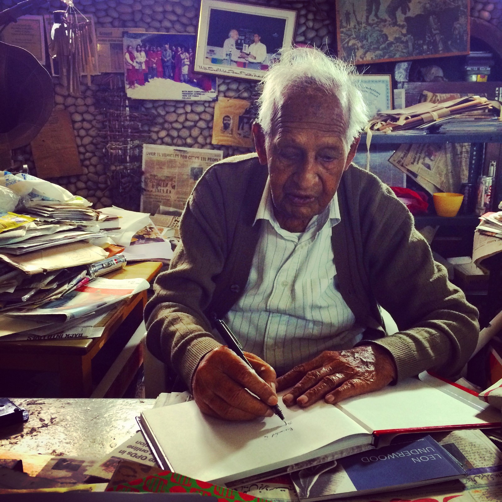 Nek Chand working in his studio An elderly Indian man draws ina sketchbook surrounded by piles of paper, photographs and other ephemera