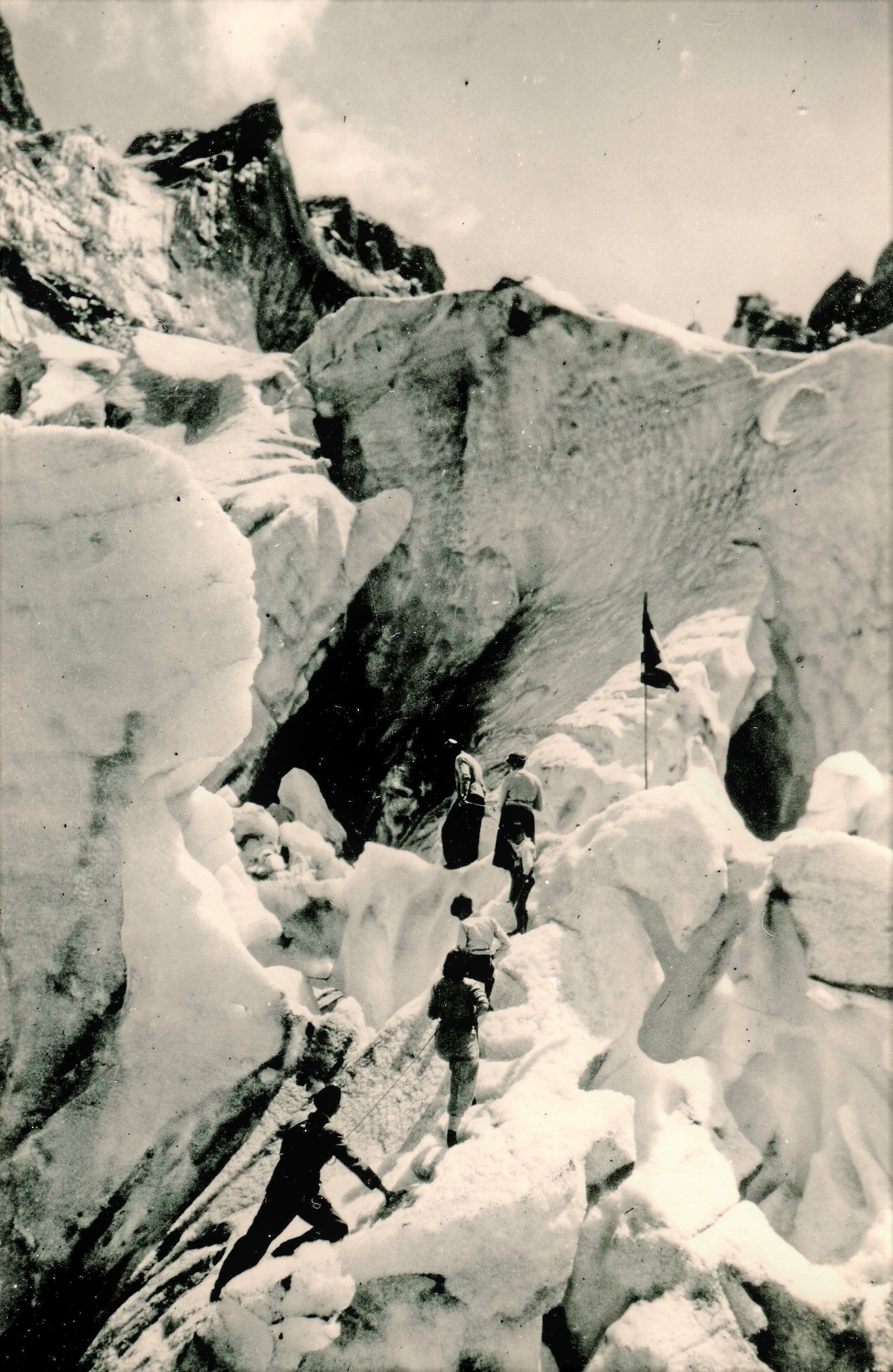 Wilhelmina Barns-Graham (second from left) climbing the Grindelwald Glacier, Switzerland A black and white photograph showing a group of six people walking up the steep sides of a glacier, tethered together by rope.