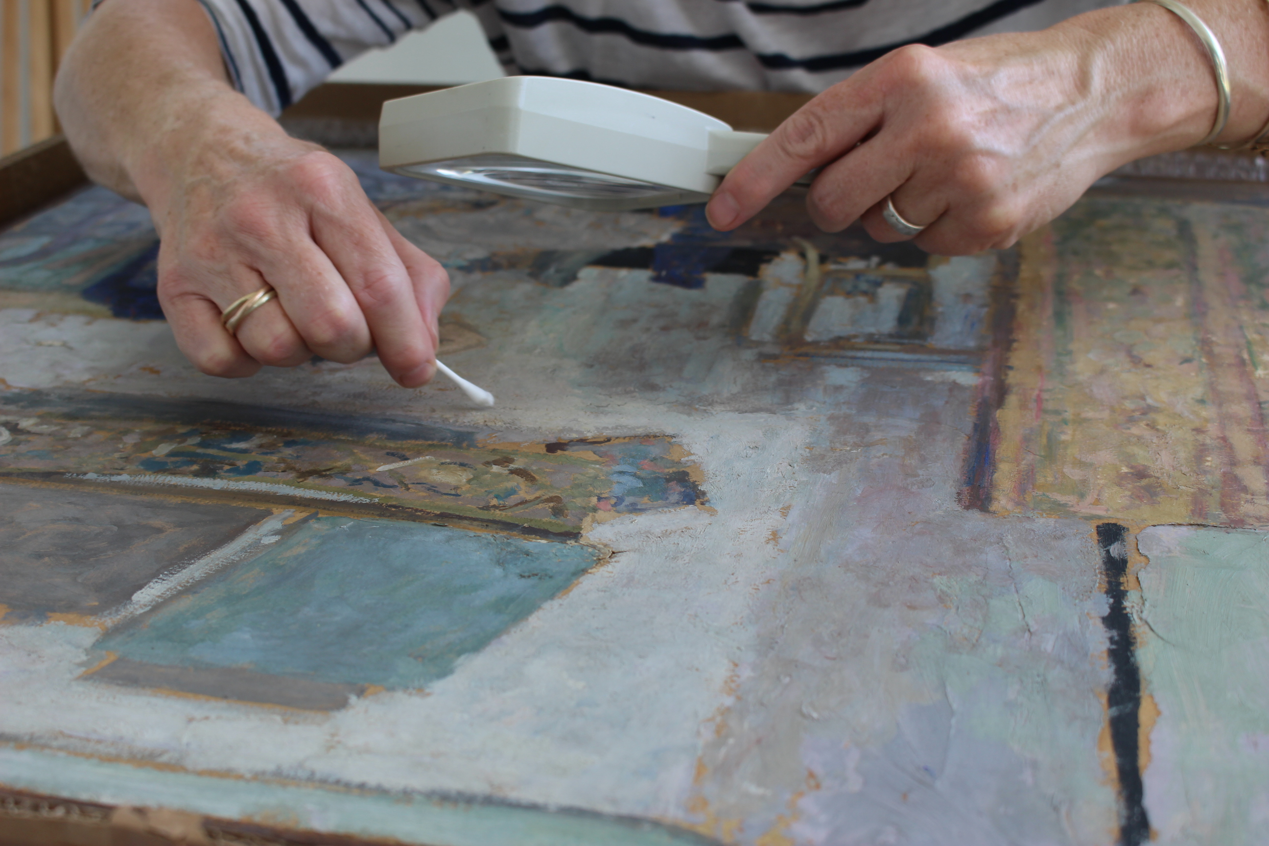 Conservator conserving painting with magnifying glass and cotton bud